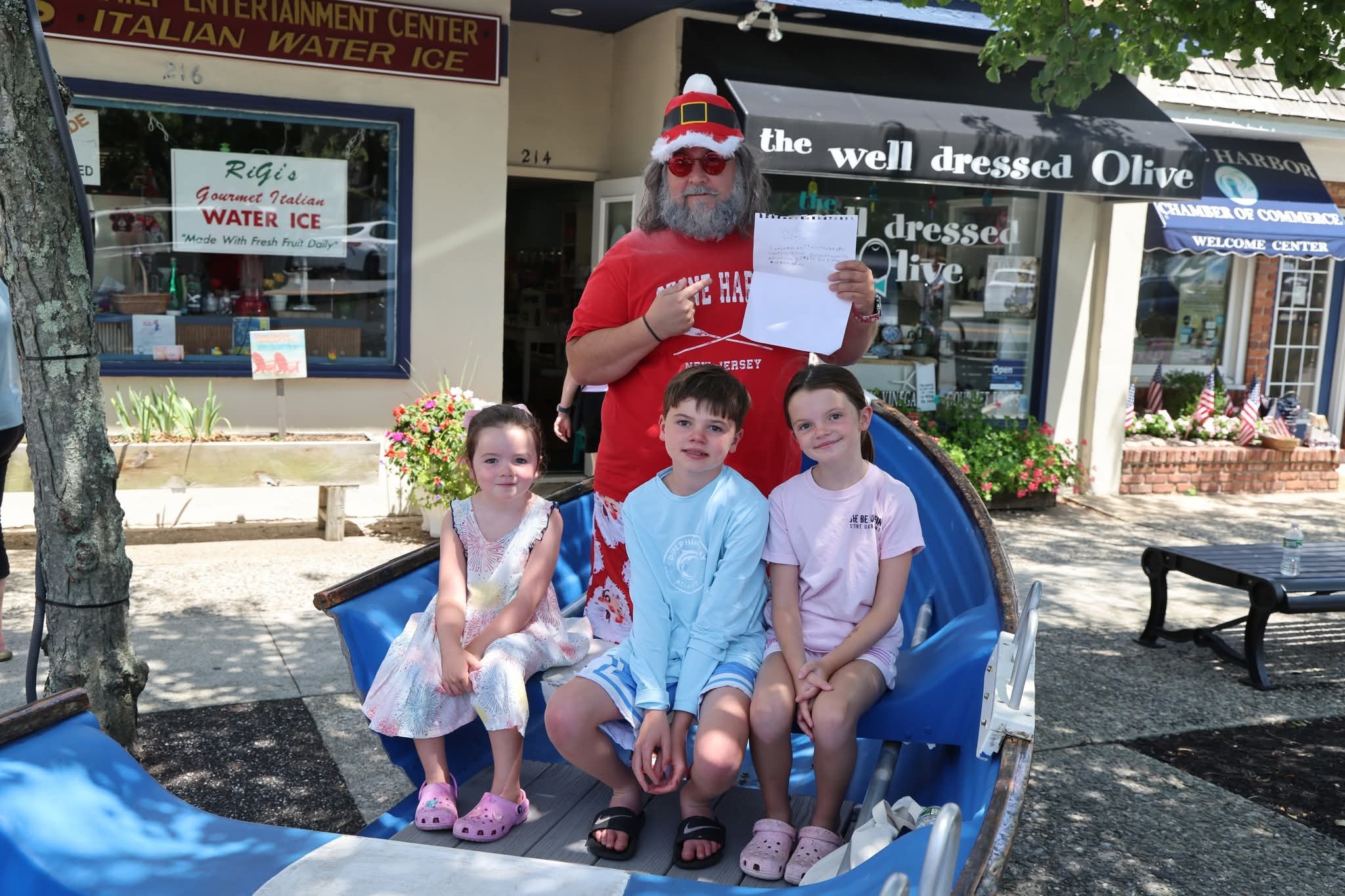 Cape May County Santa holding up a child's Christmas wish list with three kids in the Stone Harbor boat