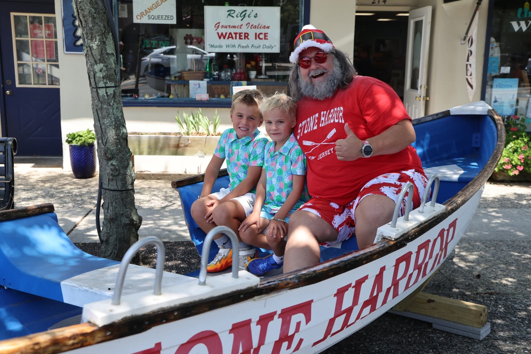 Cape May County Santa giving a thumbs up with two boys in matching floral polo shirts in the Stone Harbor boat