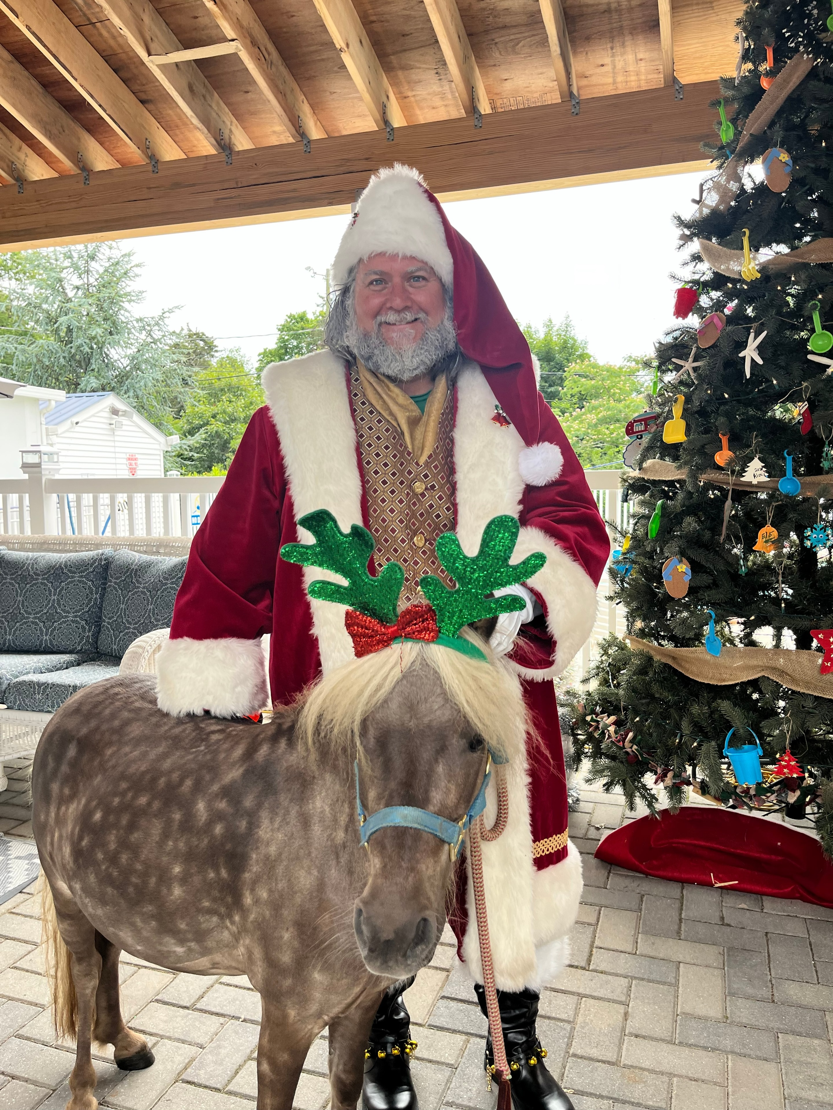 Cape May County Santa with a mini pony wearing reindeer antlers beside a beach-themed Christmas tree