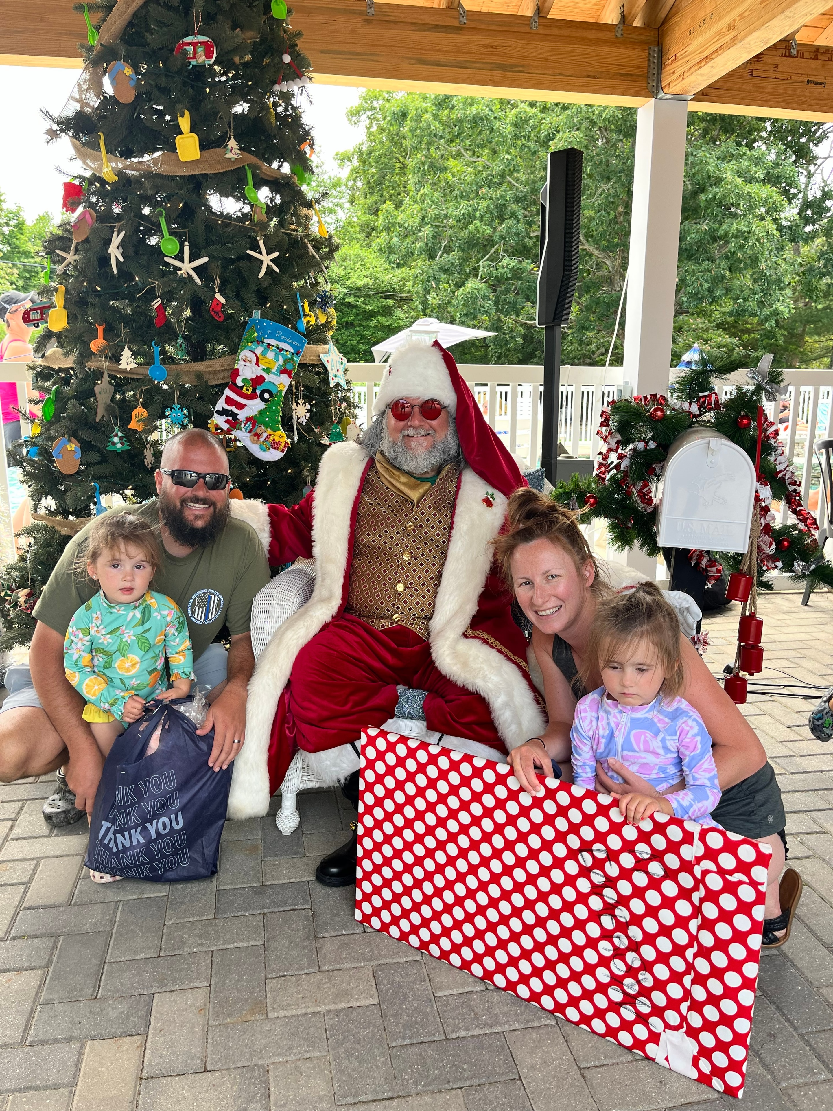 Family posing with Cape May County Santa beside a beach-themed Christmas tree at a campground pool party
