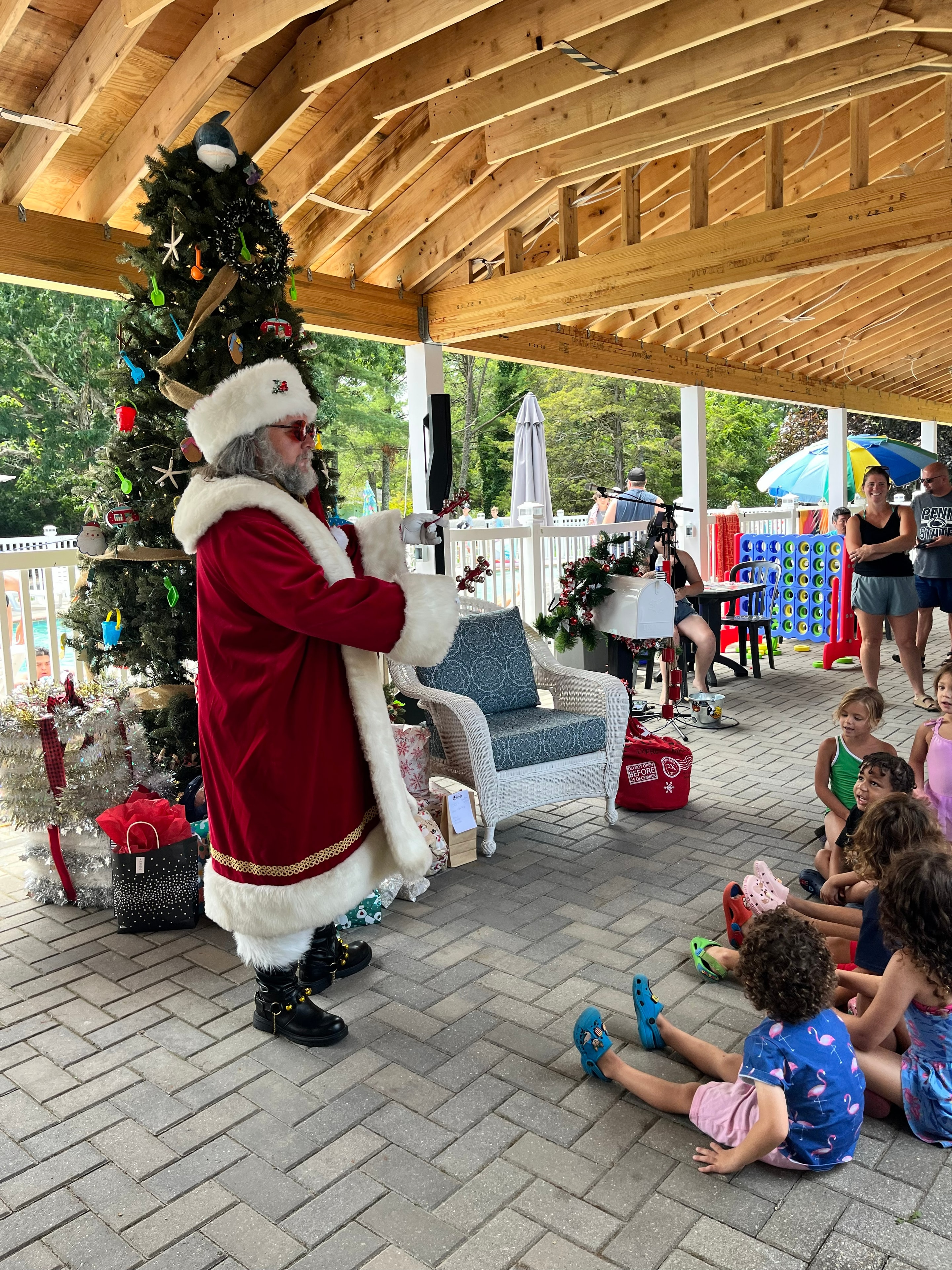 Cape May County Santa pointing at a Christmas stocking on a beach-themed tree while children sit on the patio