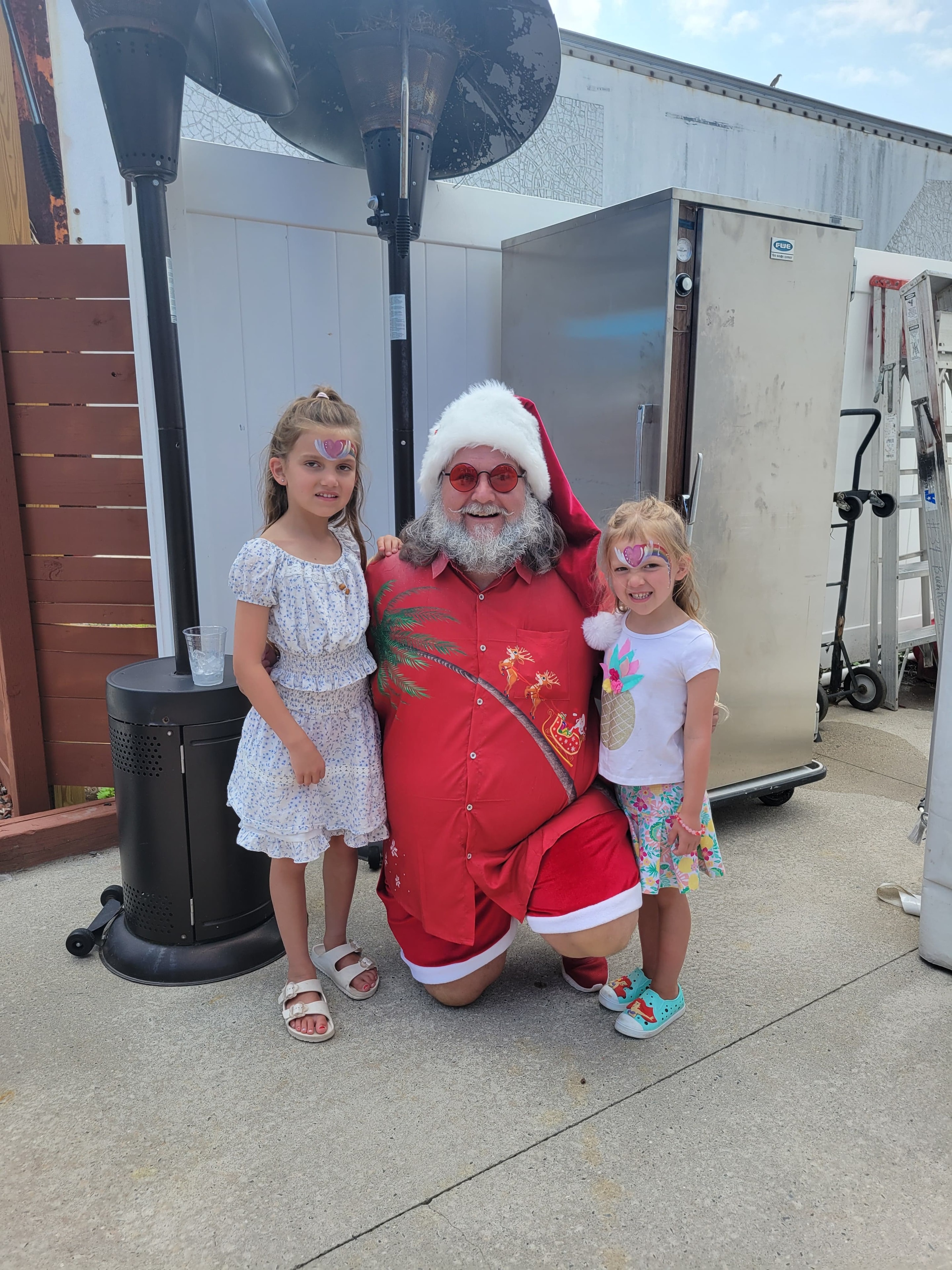 Cape May County Santa kneeling with two face-painted girls at an outdoor event