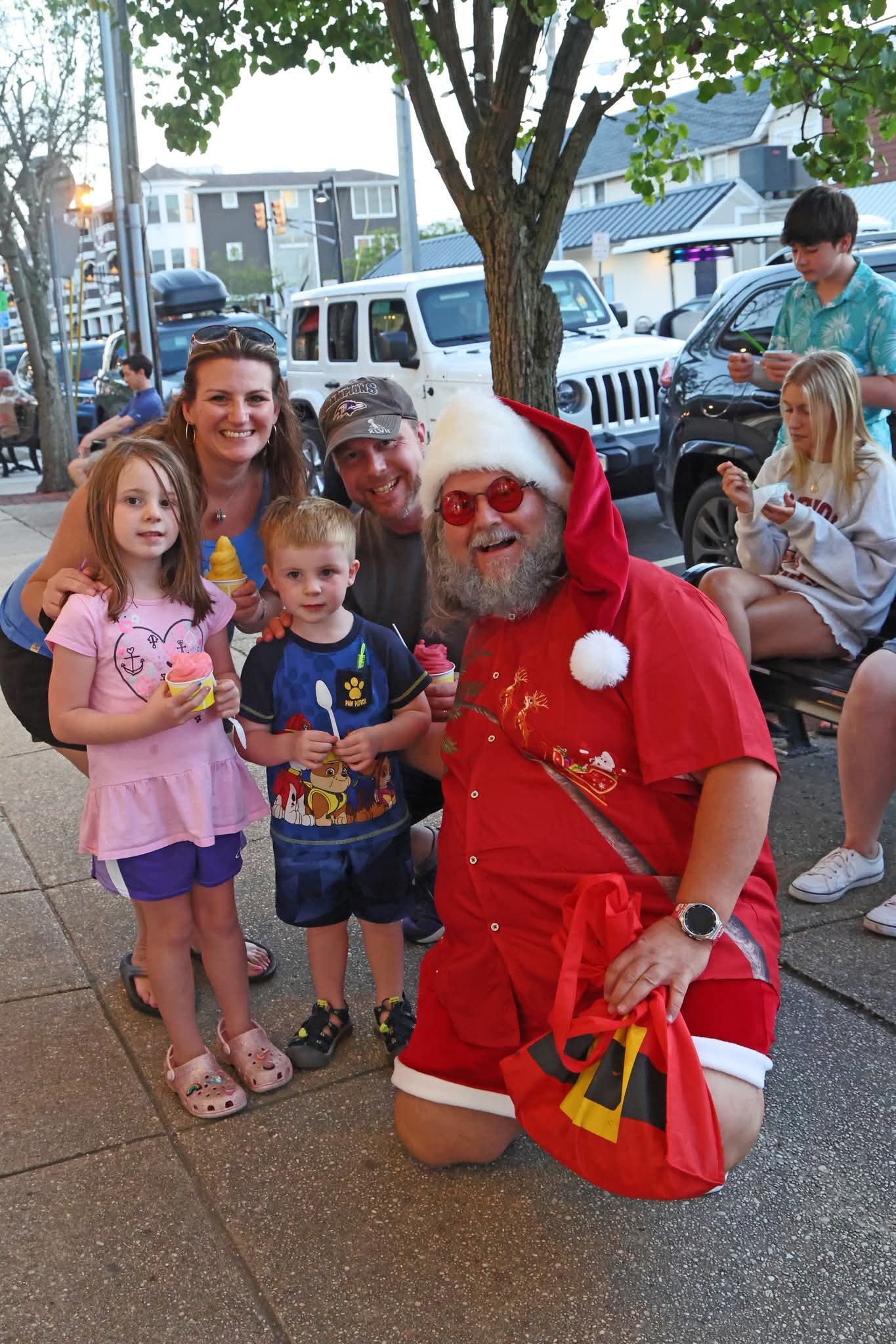 Cape May County Santa kneeling with a family of four holding water ice cups on the sidewalk