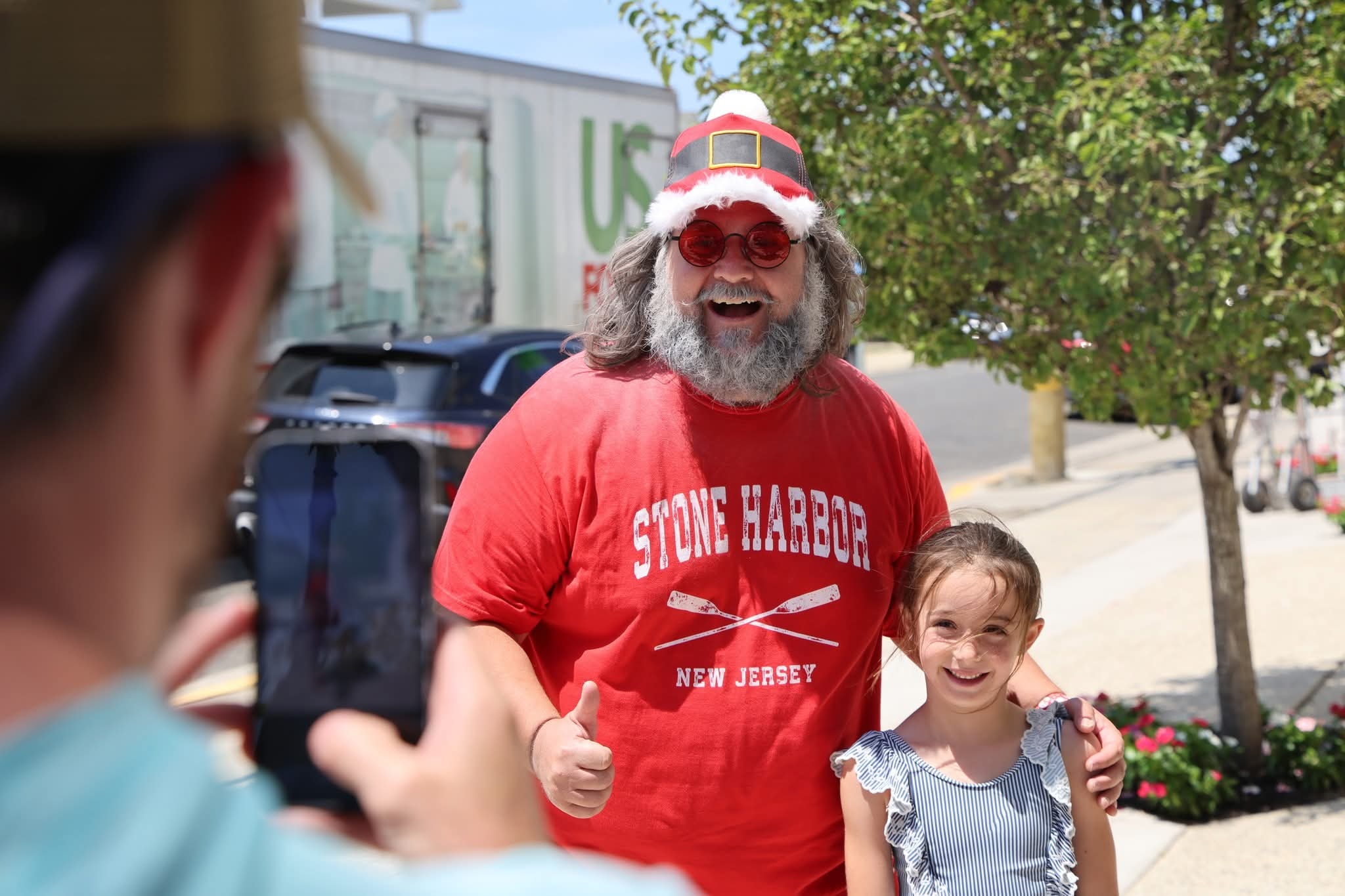 Cape May County Santa giving a thumbs up while a dad photographs him with a young girl on the street